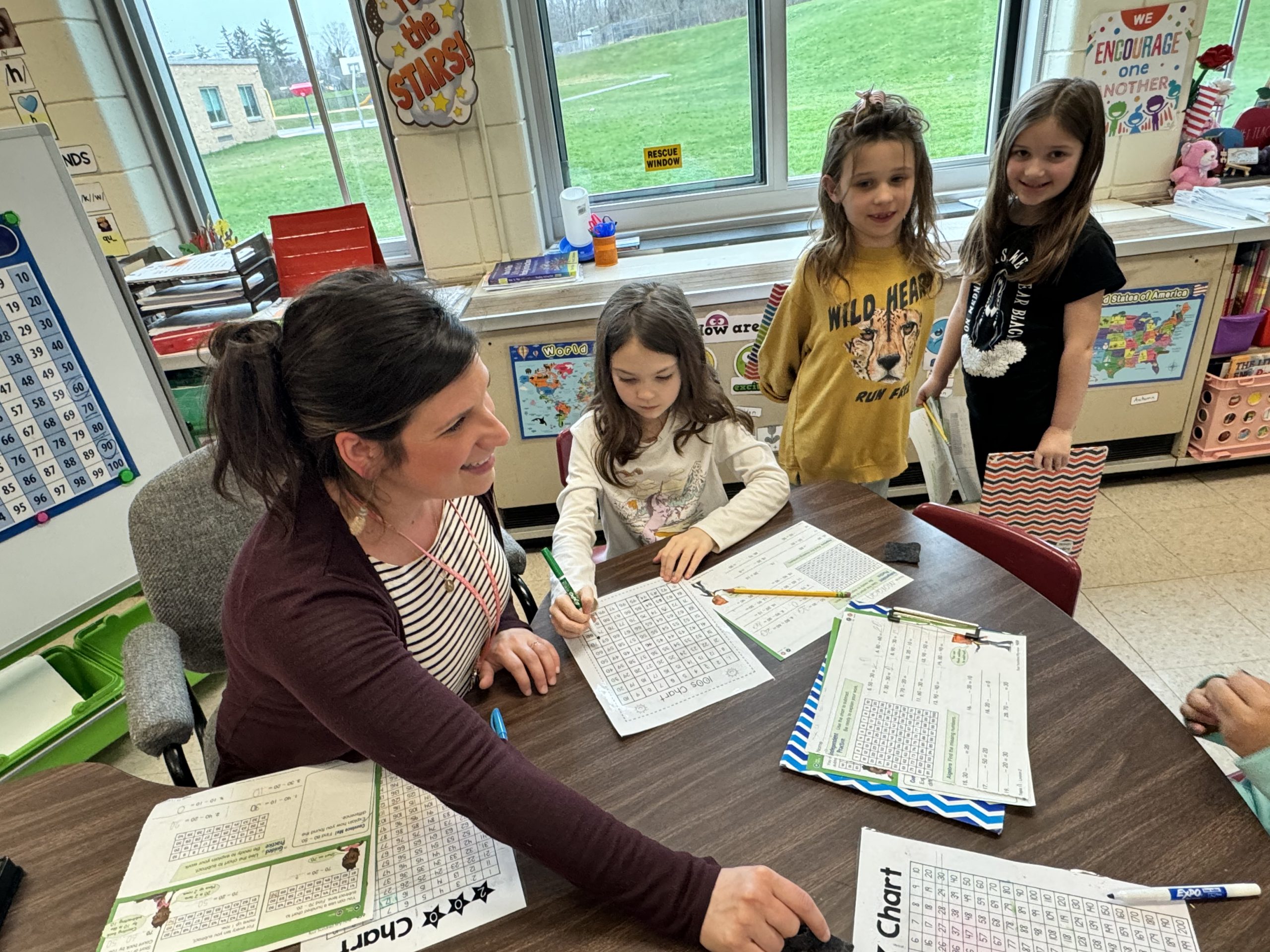 Three students gather at an elementary teacher's desk