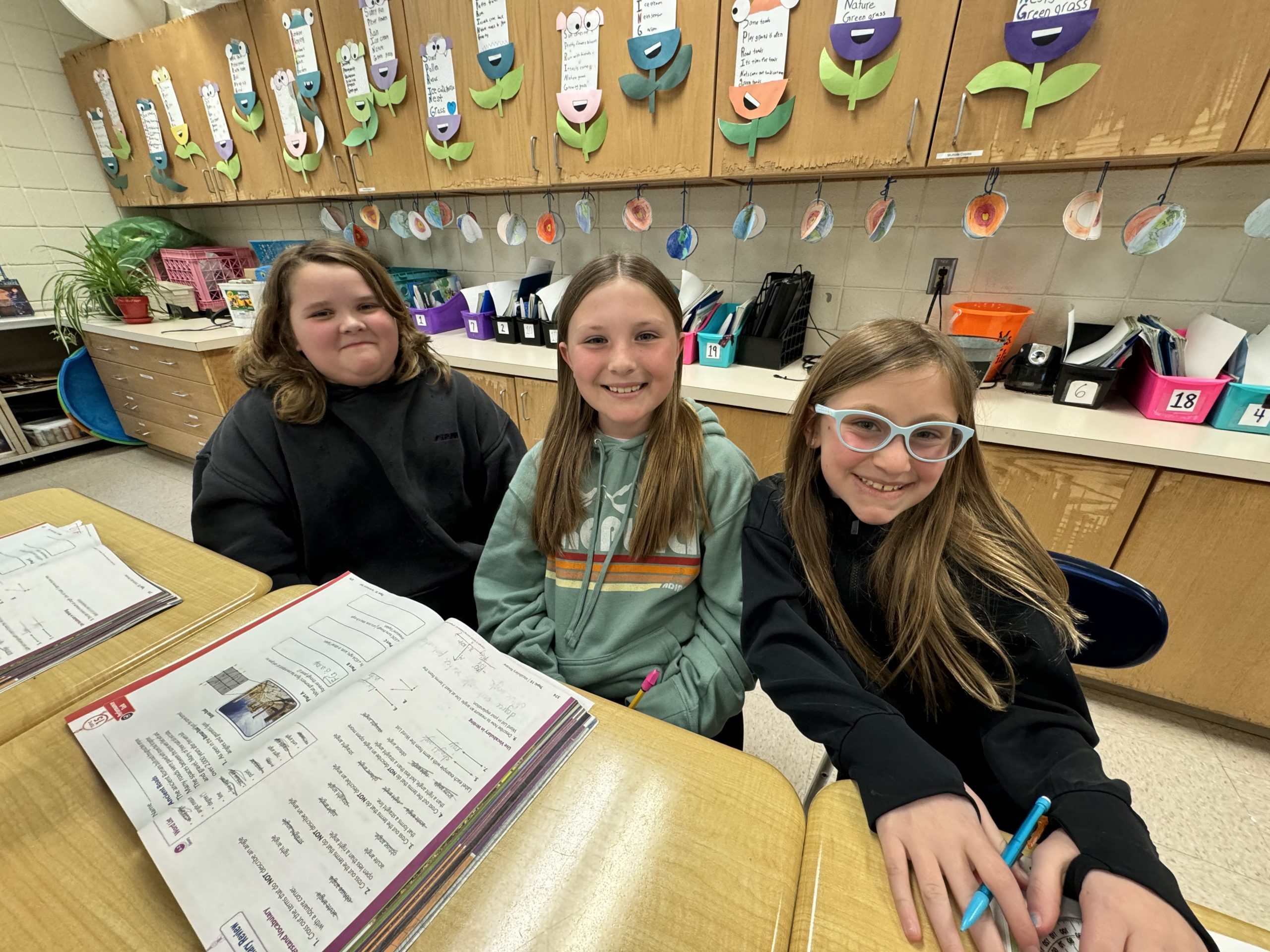 Three elementary school students pose with smiles in the classroom