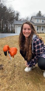 A student poses with a flamingo on her front lawn.
